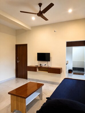 A bedroom with a bed, a desk, a television, and a ceiling fan. - Sri Abirami Homestays - Residency (Tiruvannamalai)