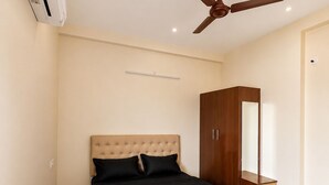 A bedroom with a bed, a ceiling fan, a wardrobe, and an air conditioning unit.