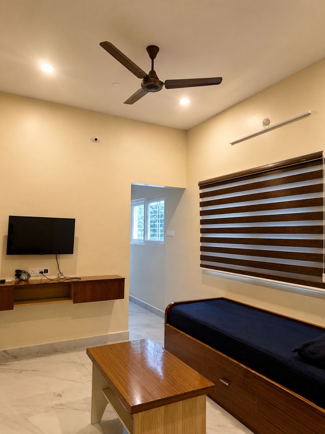 Una sala de estar moderna con ventilador de techo, televisor de pantalla plana, banco de madera y sofá con persianas horizontales.