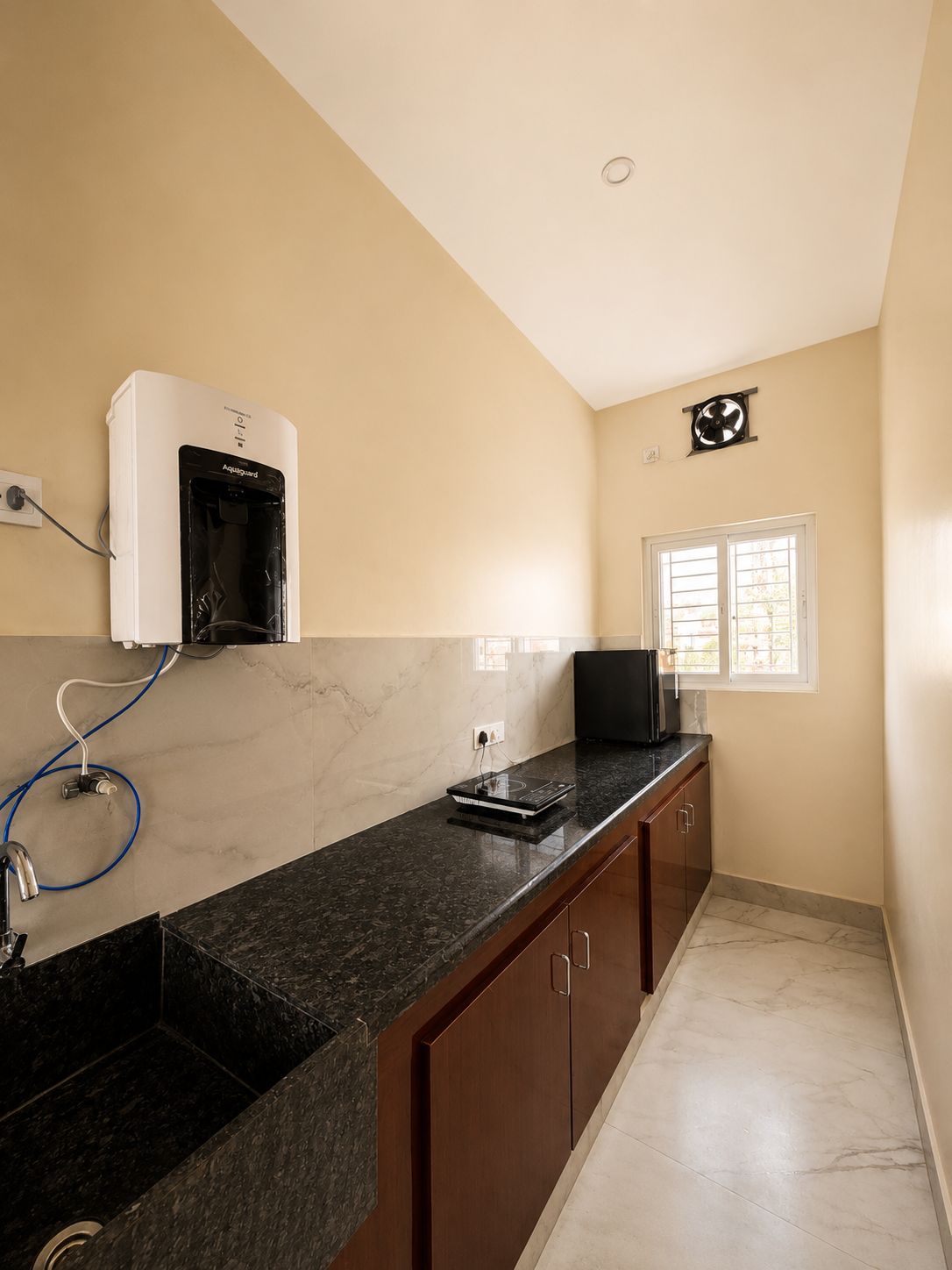 A kitchen with a black countertop, a built-in microwave, and a water heater on the wall.