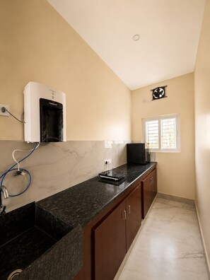 A kitchen with a black countertop, a built-in microwave, and a water heater on the wall. - Sri Abirami Homestays - Residency (Tiruvannamalai)