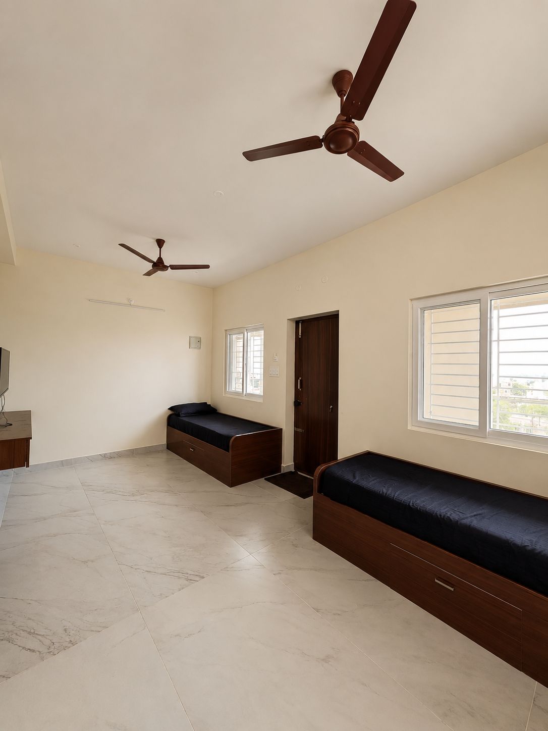 Una habitación amplia con dos camas, un ventilador de techo, una ventana y una puerta.