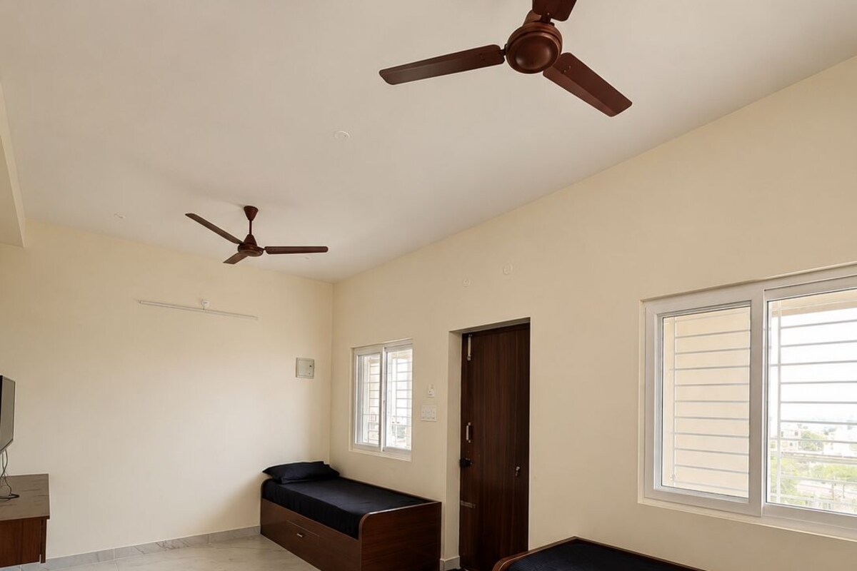 Una habitación amplia con dos camas, un ventilador de techo, una ventana y una puerta.