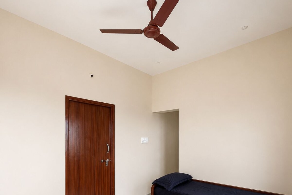 Un dormitorio con puerta de madera, una cama con colchón oscuro y un ventilador de techo.