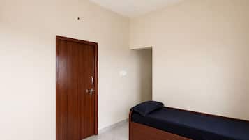 Un dormitorio con puerta de madera, una cama con colchón oscuro y un ventilador de techo.