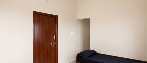 Un dormitorio con puerta de madera, una cama con colchón oscuro y un ventilador de techo.
