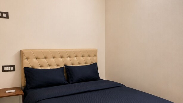A bedroom with a tufted headboard, a dark-colored bedspread, and a nightstand with a remote control.