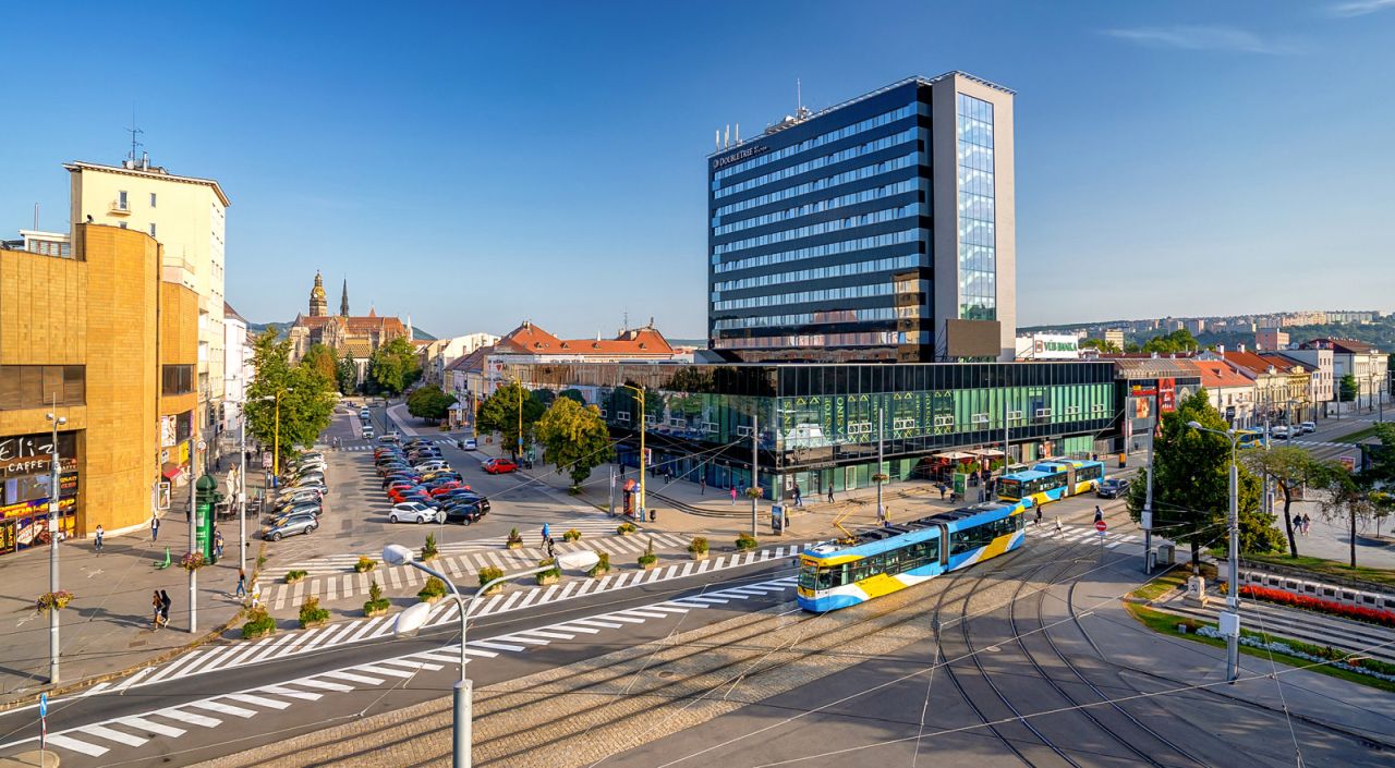 A tram station with a modern building, a tram, and a crosswalk.
