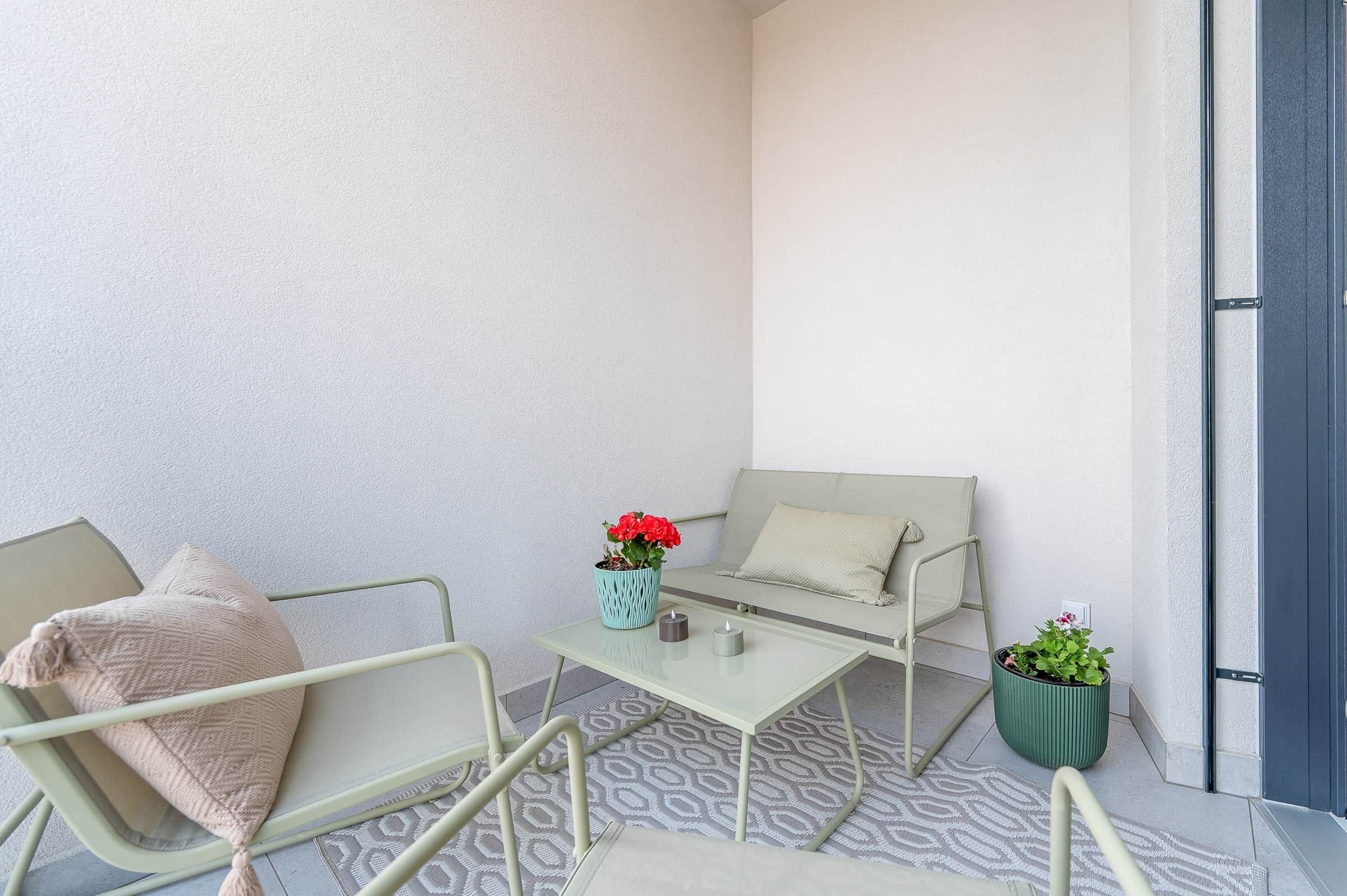 Een balkon met een bank, stoelen, een klein tafeltje en plantenpotten.