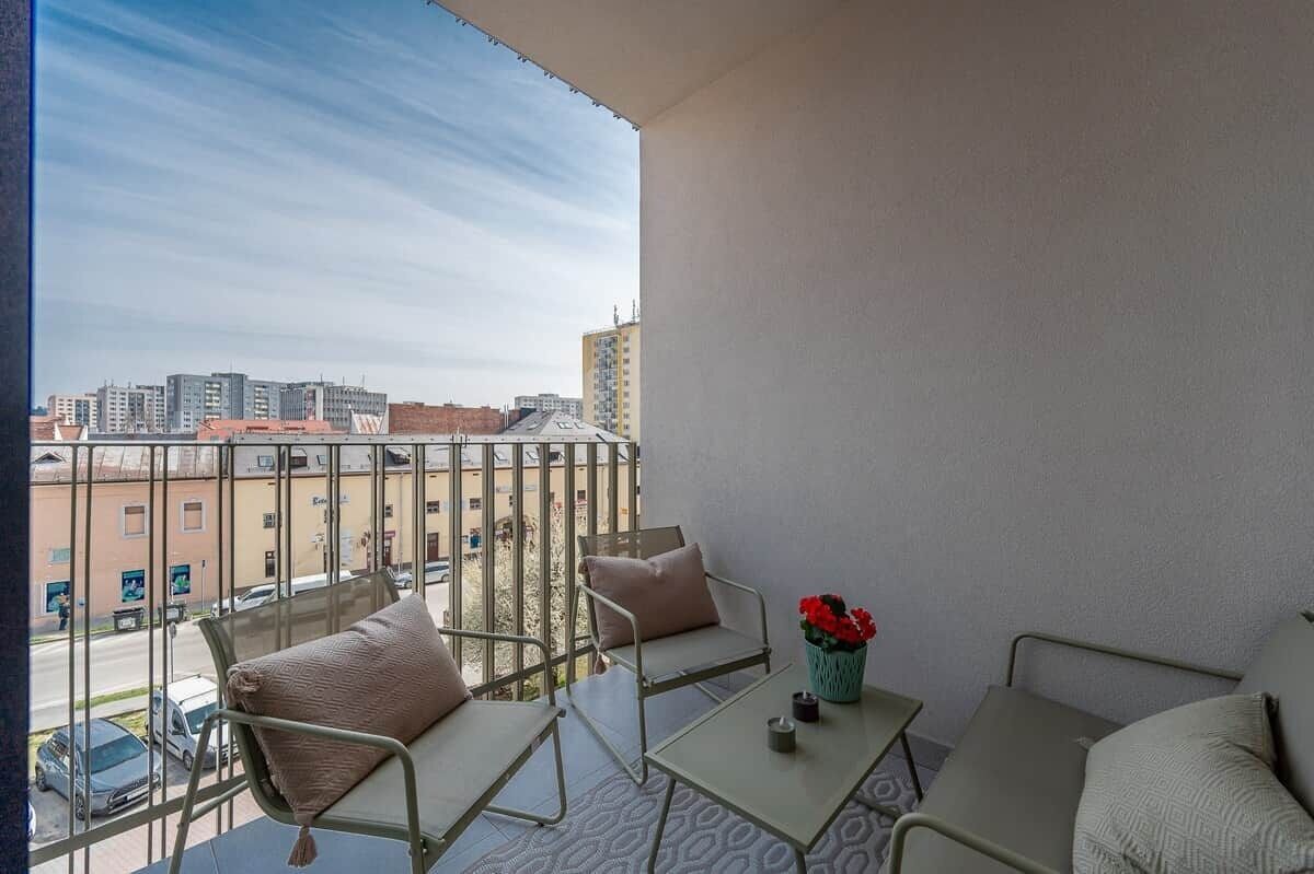 A balcony with a view of a cityscape, featuring a sofa, a table, and a vase with flowers.