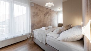 Ein Schlafzimmer mit einem Bett, einem Heizkörper, einem Fenster mit durchsichtigen Vorhängen und einer strukturierten Wand.
