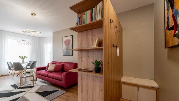 Ein modernes Wohnzimmer mit einem roten Sofa, einem Holzregal und einer Essecke mit Tisch und Stühlen.