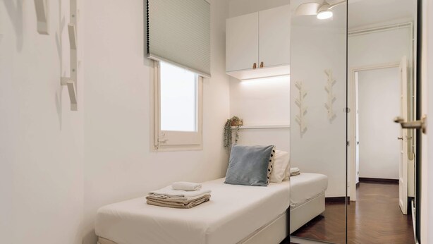 A bedroom with a bed, a bedside table, a window, and a mirror. - Enjoy Apartments Paz - Bright apartment near Sagrada Familia (Barcelona)