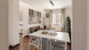 A dining area with a white table, grey chairs, a cityscape artwork, a television, and a plant. - Enjoy Apartments Paz - Bright apartment near Sagrada Familia (Barcelona)