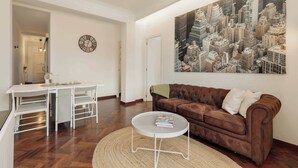 A living room with a brown sofa, a round coffee table, a dining table with chairs, and a cityscape painting on the wall. - Enjoy Apartments Paz - Bright apartment near Sagrada Familia (Barcelona)