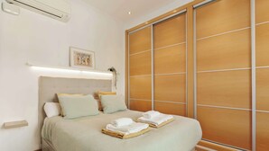 A hotel room with a bed, pillows, a bedside table, an air conditioning unit, a framed picture on the wall, and a sliding wooden door. - Enjoy Apartments Paz 2 - Bright apartment near Sagrada Familia (Barcelona)