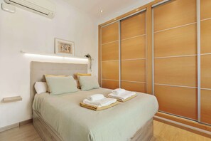 Habitación de hotel con cama, almohadas, mesita de noche, equipo de aire acondicionado, un cuadro en la pared y puerta corredera de madera.