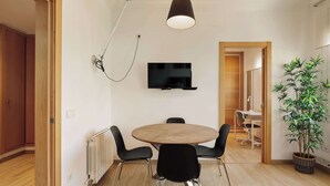 A modern dining area with a round table, four chairs, a wall-mounted TV, and a hanging light fixture. - Enjoy Apartments Paz 2 - Bright apartment near Sagrada Familia (Barcelona)