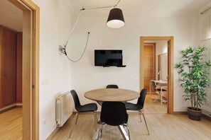 Un comedor moderno con una mesa redonda, cuatro sillas, un televisor montado en la pared y una lámpara colgante.