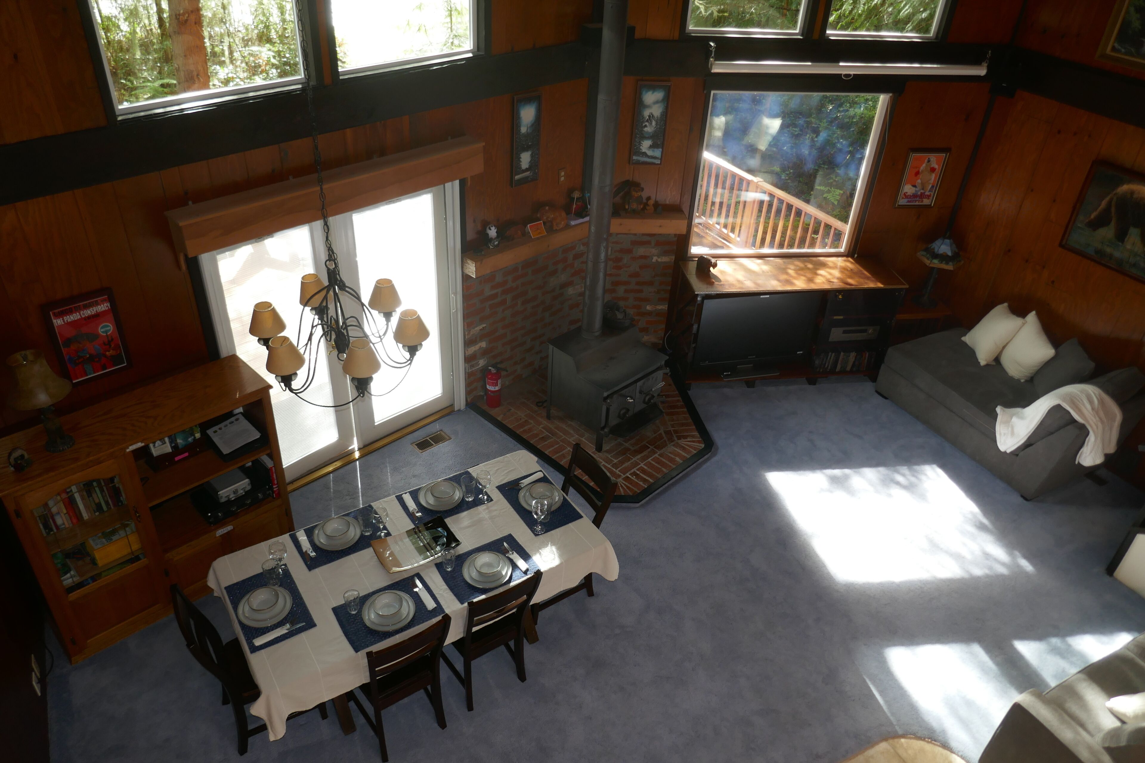 A dining area with a table set for four, a fireplace, and a sofa in a room with wooden walls and large windows.