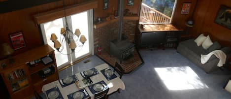 A dining area with a table set for four, a fireplace, and a sofa in a room with wooden walls and large windows.