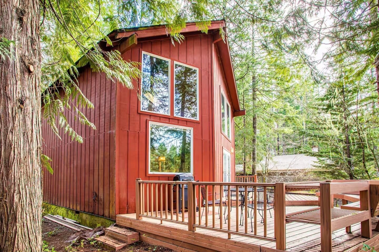 Une cabane rouge dotée d’une terrasse et offrant une vue sur la forêt.
