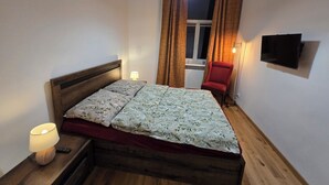 A single bed with a wooden frame and floral bedding, a red chair, a bedside lamp, and a television on the wall. - Lazienki park Bagatela street Top floor apartment with lift (Warszawa)