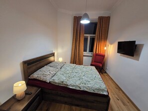 A single bed with a wooden frame and floral bedding, a red chair, a bedside lamp, and a television on the wall. - Lazienki park Bagatela street Top floor apartment with lift (Warszawa)