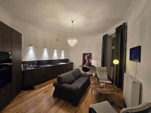 A modern living room with a dark sofa, a round coffee table, and a dining area with a kitchen counter. - Lazienki park Bagatela street Top floor apartment with lift (Warszawa)