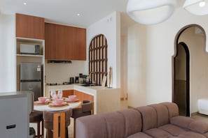 A modern kitchen with built-in appliances, a dining area with a round table and chairs, and a living area with a sofa. - Kamala Villa by Betterplace (Pecatu)