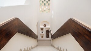 A staircase with wooden handrails and a white wall with a small shelf containing decorative items. - Kamala Villa by Betterplace (Pecatu)