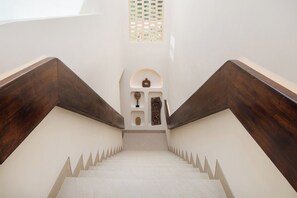 A staircase with wooden handrails and a white wall with a small shelf containing decorative items. - Kamala Villa by Betterplace (Pecatu)