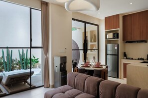 A modern living room with a sofa, a dining area with a table set for two, and a kitchen with a refrigerator and microwave. - Kamala Villa by Betterplace (Pecatu)