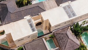A multi-story building with a swimming pool, a covered patio, and a rooftop terrace. - Kamala Villa by Betterplace (Pecatu)