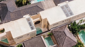 A multi-story building with a swimming pool, a covered patio, and a rooftop terrace. - Kamala Villa by Betterplace (Pecatu)