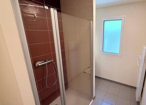 Ein Badezimmer mit Duschkabine aus Glas, einer weißen Toilette und einem Fenster mit Blick.
