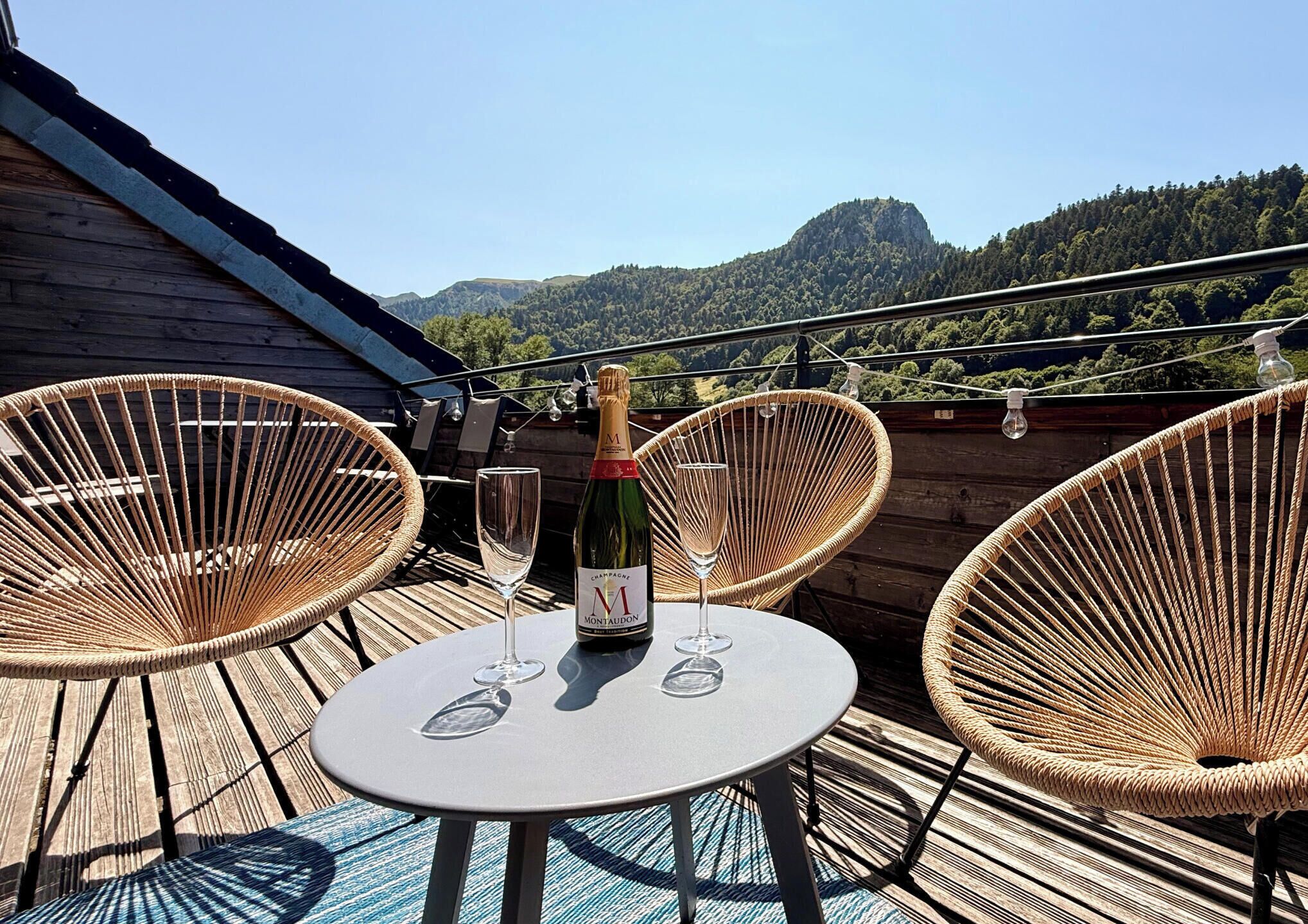 A terrace with wicker chairs, a round table, and a bottle of champagne.