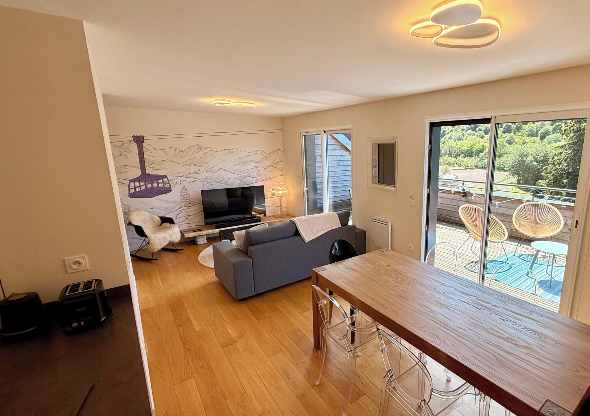 Una sala de estar moderna con un sofá, televisor y un comedor con mesa de madera.