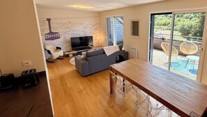 A modern living room with a sofa, TV, and a dining area with a wooden table. - Le Belvédère de La Montille (sleeps 6) (Mont-Dore)