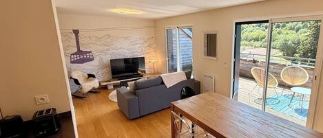 A modern living room with a sofa, TV, and a dining area with a wooden table.