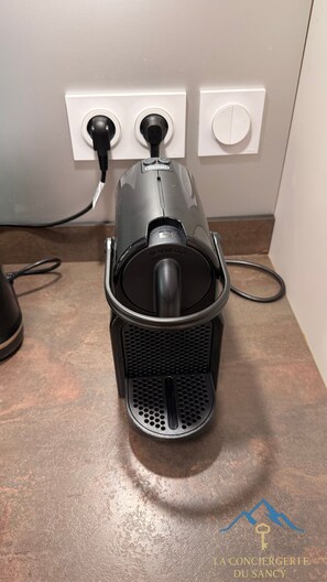En Nespresso-kaffemaskin står på en bänkskiva, med ett eluttag och en strömbrytare synliga i bakgrunden.