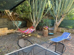 Eine Terrasse mit einer Hängematte, zwei gestreiften Liegestühlen, einem Metalltisch und einem Blumentopf.