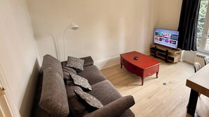A living room with a sofa, a red coffee table, a floor lamp, and a television. - Fenestre La Bourboule Park (4 people) (La Bourboule)