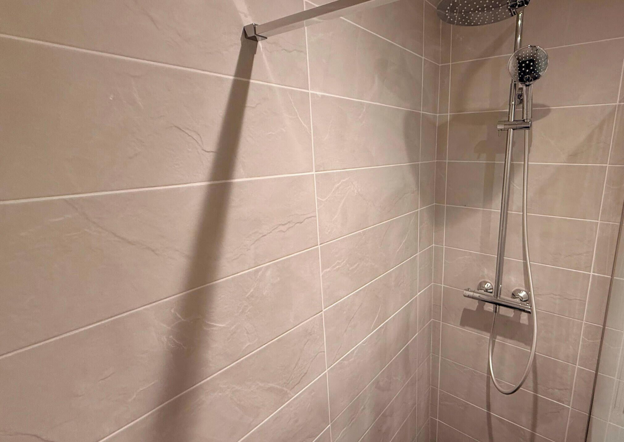 A shower area with a handheld showerhead and a wall-mounted control panel.