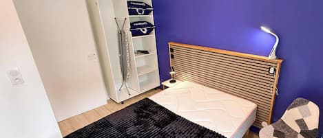 A bedroom with a bed, a wardrobe, a desk with a lamp, and a chair.