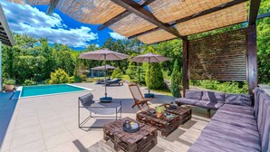 An outdoor patio with a pool, lounge chairs, a sofa, and wooden tables. - Villa Sandra by Villas Guide (Veli Brgud)