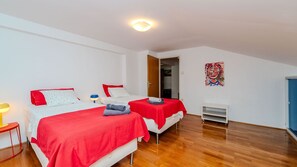 Ein Zimmer mit zwei Betten, Holzboden, einem Bild an der Wand und einer Tür zu einem anderen Raum.