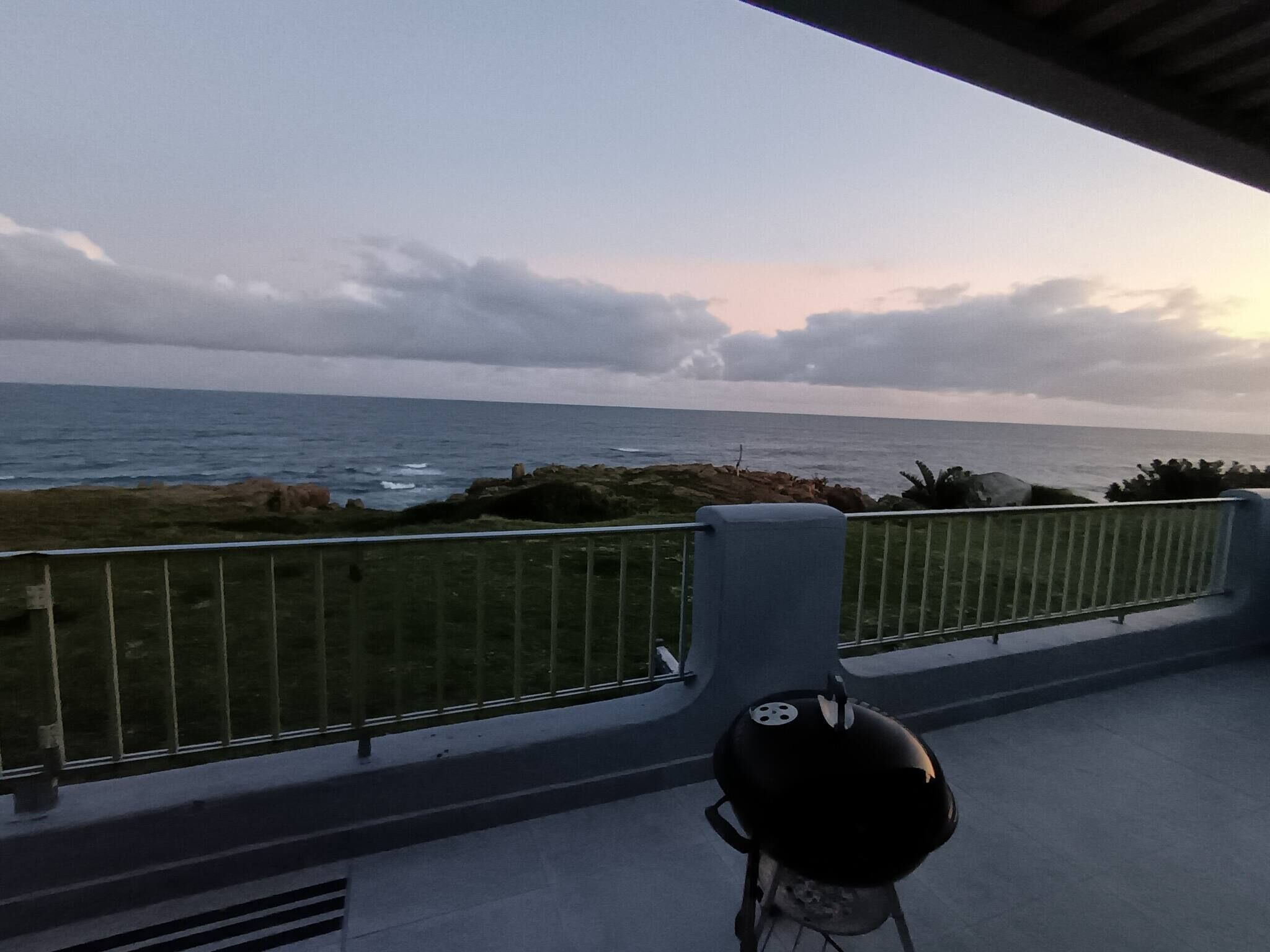 A balcony with a view of the ocean, a grill, and a railing.
