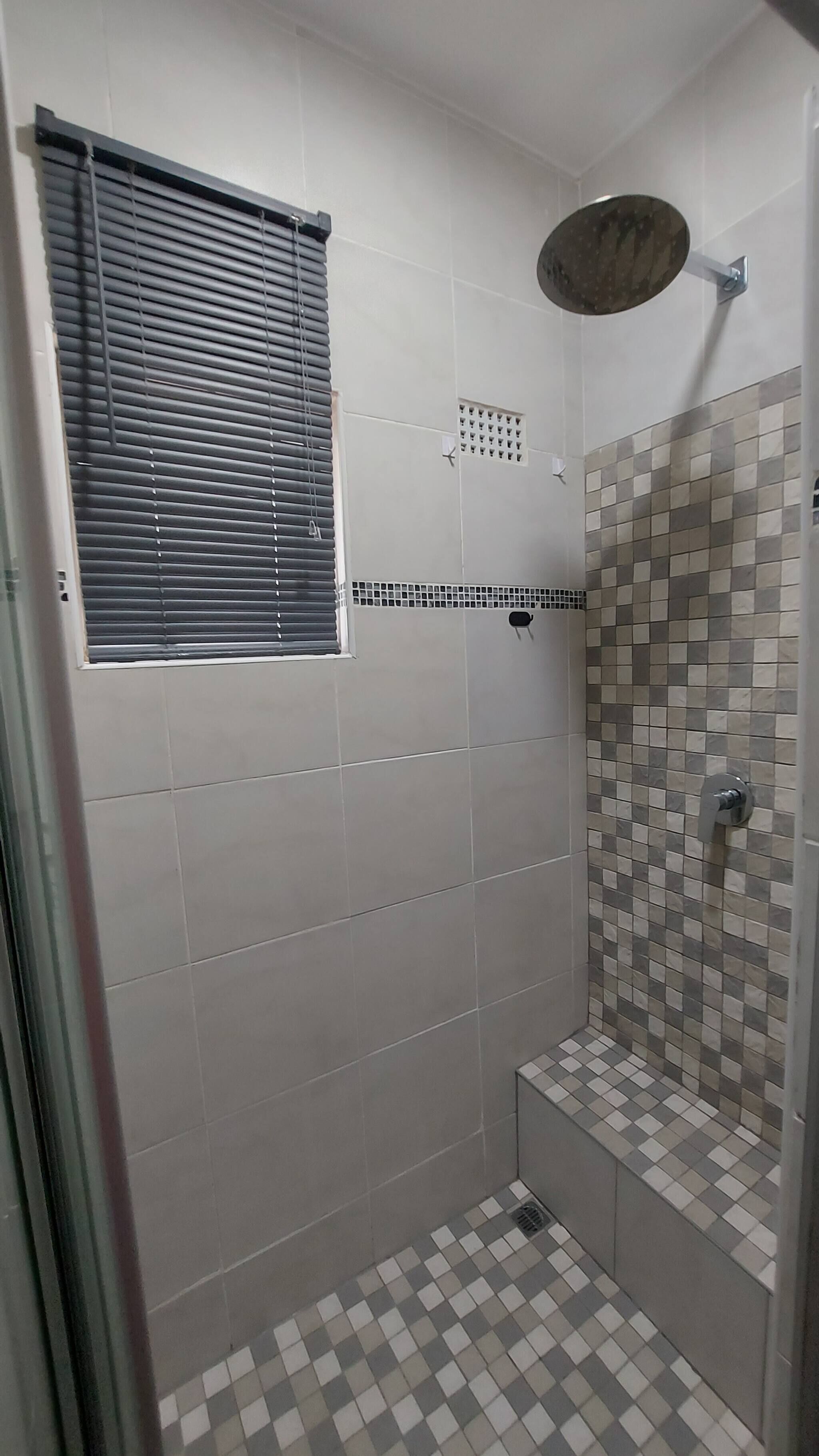 A shower with a tiled floor and a window with blinds.