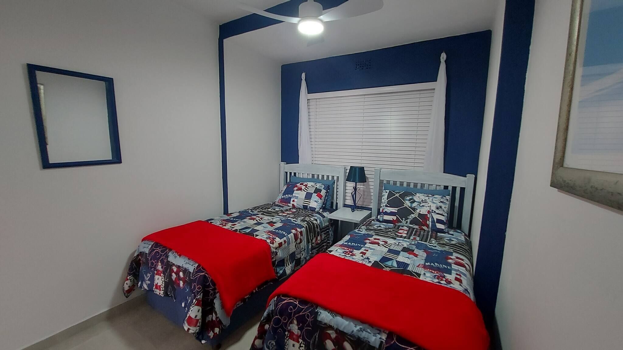 A bedroom with two single beds, a ceiling fan, a window with blinds, and a framed picture on the wall.